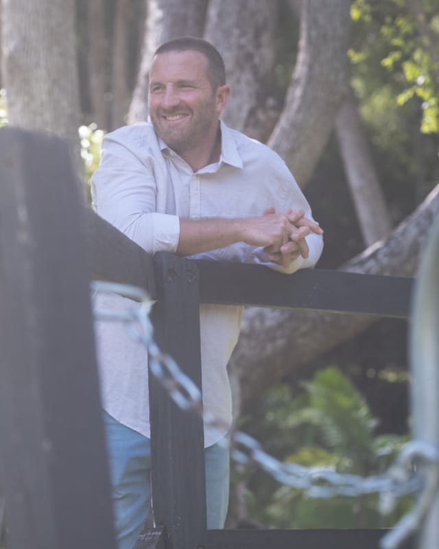 Rich Muir leaning on a timber fence in the Currumbin Valley, smiling