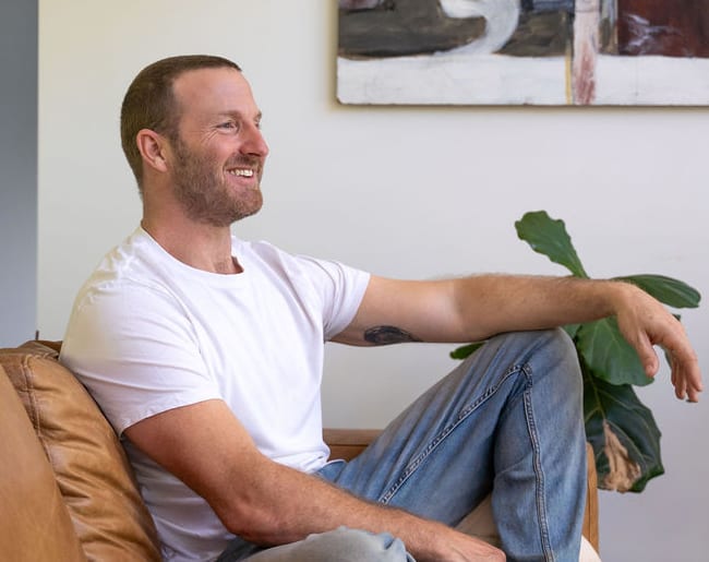 Rich Muir smiling in conversation on a tan leather sofa